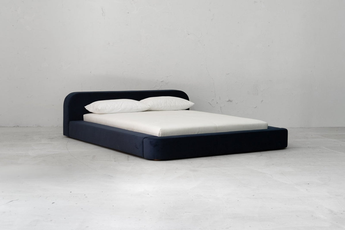 The Spire Bed by Sun at Six. A low platform upholstered bed. Shown in Navy velvet